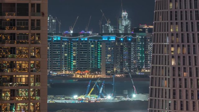 Aerial view to Dubai marina skyscrapers with construction site and Palm Jumeirah Island on background night timelapse. Building of new ship terminal