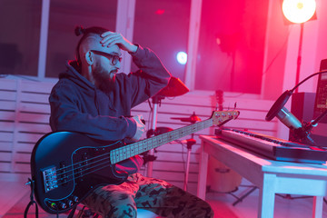 Fototapeta na wymiar Create music and a recording studio concept - Bearded funny man guitarist recording electric bass guitar track in home studio