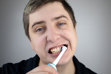 A man brushes his teeth with an electric brush while looking at the camera, as if looking in a...