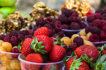 Ripe fruits in glasses for street sale. Red and white raspberries, strawberries figs, nuts. Travel and adventure.