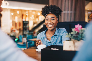 A young woman sitting in a cafe with two male friends, chatting.