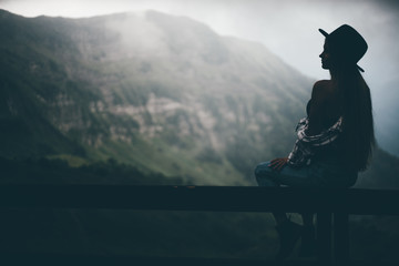 Stylish hipster girl with hat looking to the mountains. A view from the back of a girl in a hat on a mountain and admires the beautiful view. Travel and wanderlust. Amazing moment.