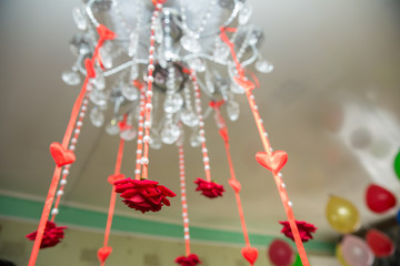 A red ribbon shades out of Chandelier. Engagement decor . Artificial red heart and roses hanging from the laurel.