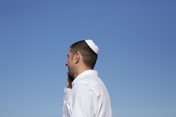 portrait of a young jew in kippah talking on a mobile phone on a blue sky background. Business concept.