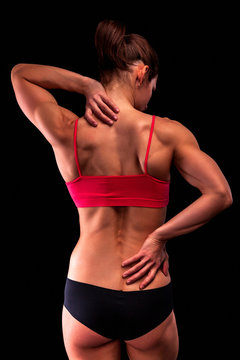 Bodybuilder woman suffers from pain in her back and neck after workout, black background