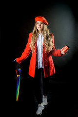 beautiful blond female with rainbow umbrella . Emotional teen girl in autumn or spring red coat and take on a black background in the studio