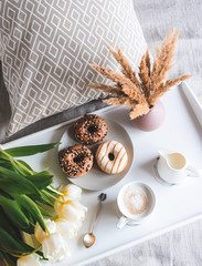 Breakfast in bed, cup with cappuccino, doughnuts, flowers white tulips, morning concept, linen bed sheets, woman's day