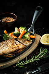 Fried fish in a frying pan with vegetables