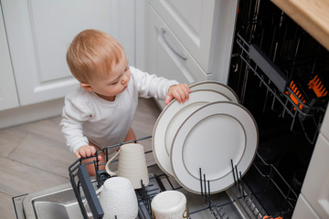 kid loads the dishwasher with plates and his toys. little helper