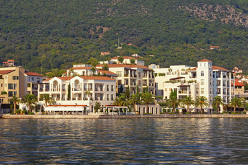 Fototapeta na wymiar Mediterranean town at foot of mountain. Beautiful view of embankment of Tivat city from sea on sunny summer day. Montenegro, Adriatic Sea, Kotor Bay
