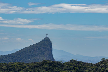 Fototapeta na wymiar Corcovado mountain in Rio de Janeiro, Brazil, seen from the Pedra Bonita viewpoint with part of the Tijuca forest in the foreground and mountain peak and Christ statue in the back against a blue sky