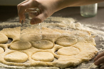 Woman making holes in raw homemade doughnuts pastry on the kitchen table, preparations for Fat Thursday holiday, european tradition before Easter