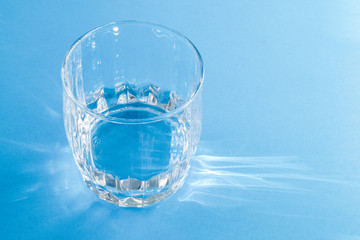 A glass with clean clear clear water stands on a blue surface. Hard light.