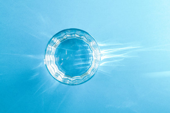A glass with clean clear clear water stands on a blue surface. Hard light. View from above.