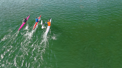 Aerial drone photo of athletes competing in canoe race in tropical lake with emerald waters