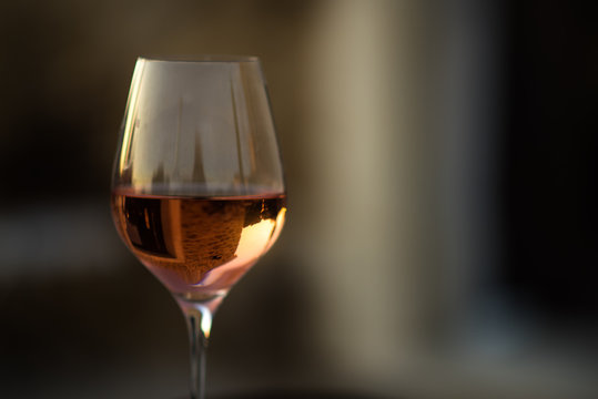 Picture in low key of glass of rose wine with reflection of old stone traditional provencal house in it. Rose wine in Provence, France. Light alcoholic drink