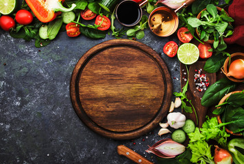 Fresh healthy food cooking or salad making ingredients on dark background with rustic wooden board. Diet or vegetarian food concept. Top view, copy space