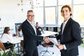 Two colleagues handshaking after meeting in office room