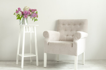A cozy armchair and a bouquet of lilacs. A place to read or a cup of coffee. Cozy Scandinavian interior. Minimalism
