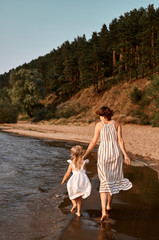 Mom with daughter holding hands, walks along the sandy shore near the water