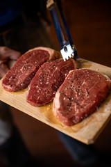 Fresh raw Prime Black Angus beef steaks on wooden board: Tenderloin, Denver Cut, Striploin, Rib Eye.uncooked Delicious beef steak cutting board.seasoning and meat fork on a table