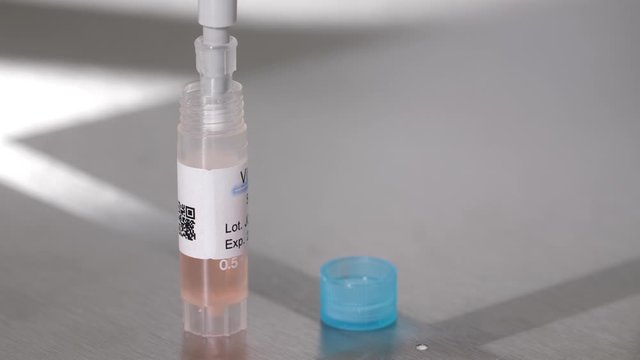 Close-up of plastic bottle with cryoprotectant substance standing on laboratory bench. Embryologist with pipette taking cryoprotectant to begin procedure of embryos cryopreservation in lab