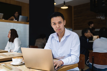 Thoughtful ethnic businessman typing on laptop in coffee shop