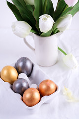 Golden Easter Eggs in ceramic egg tray with tulip on white table. Easter background or easter concept.