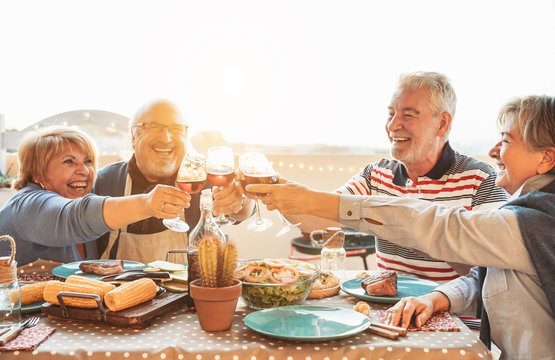 Happy senior dining and tasting red wine glasses in barbecue dinner party - Family having fun enjoying bbq at sunset time on terrace - Elderly people lifestyle and food and drink concept