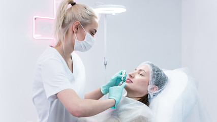 The young beautician doctor preparing to making injection in female lips. The doctor cosmetologist...