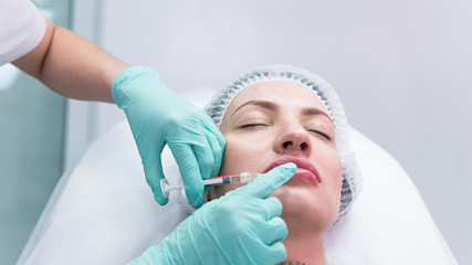 The young beautician doctor preparing to making injection in female lips. The doctor cosmetologist makes lip augmentation procedure.