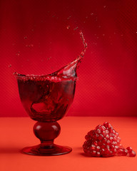 A splash of pomegranate juice in a glass and a handful of pomegranate seeds nearby. Red monochrome