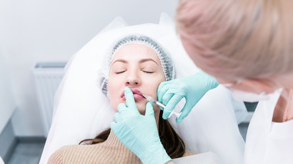 The young beautician doctor preparing to making injection in female lips. The doctor cosmetologist...