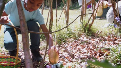 Group Of Children Wearing Bunny Ears Finding Chocolate Eggs On Easter Egg Hunt In Garden