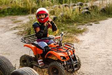 The little girl rides a quad bike ATV. A mini quad bike is a cool girl in a helmet and protective clothing. Electric quad bike electric car for children popularizes green technology. © Angelov