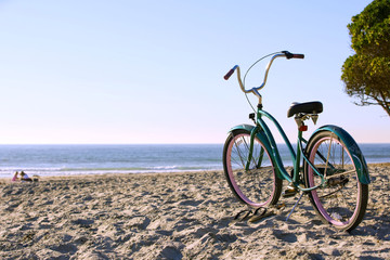 A bicycle on the beach with flip flops next to it