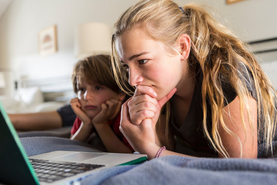 13 year old sister and her brother looking at laptop on bed