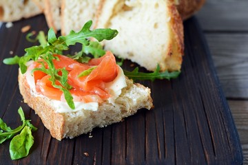Sandwich with slightly salted salmon, arugula, seeds and cottage cheese on the board. Sourdough bread toast with salted fish, smorrebrod.