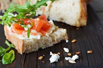 Sandwich with slightly salted salmon, arugula, seeds and cottage cheese on the board. Sourdough bread toast with salted fish, smorrebrod.