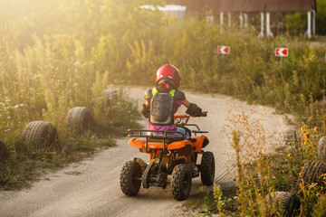 The little girl rides a quad bike ATV. A mini quad bike is a cool girl in a helmet and protective clothing. Electric quad bike electric car for children popularizes green technology.