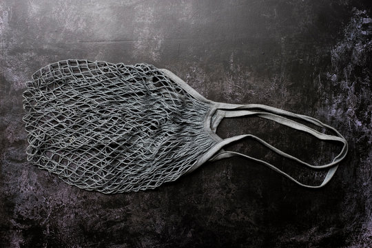 High angle close up of empty grey net bag on black background.