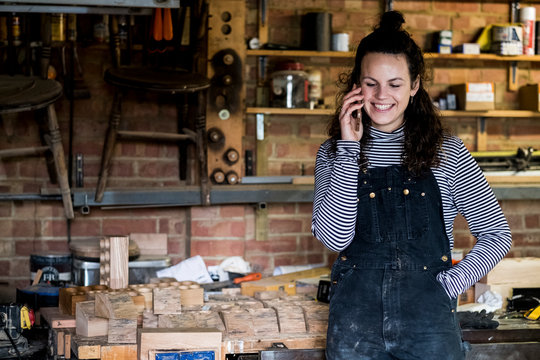 Smiling young woman talking on smart phone in workshop