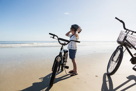 A boy putting on a cycle helmet on the beach, St. Simon's Island, Georgia,St Simon's Island