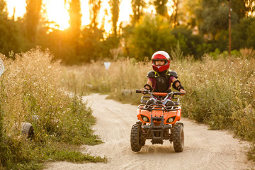 The little girl rides a quad bike ATV. A mini quad bike is a cool girl in a helmet and protective...