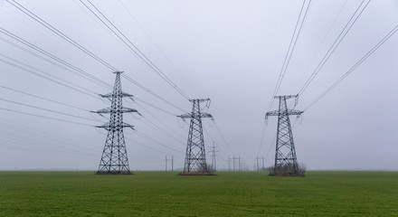 Electric network of pylons against a cloudy sky and a green meadow
