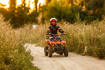 Obraz premium The little girl rides a quad bike ATV. A mini quad bike is a cool girl in a helmet and protective clothing. Electric quad bike electric car for children popularizes green technology.