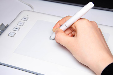 Female hands work on a graphic tablet. Hand holds stylus pen and draws. White graphic tablet. The work of a graphic designer. Girl works on a tablet connected to a laptop. Rear view from  behind