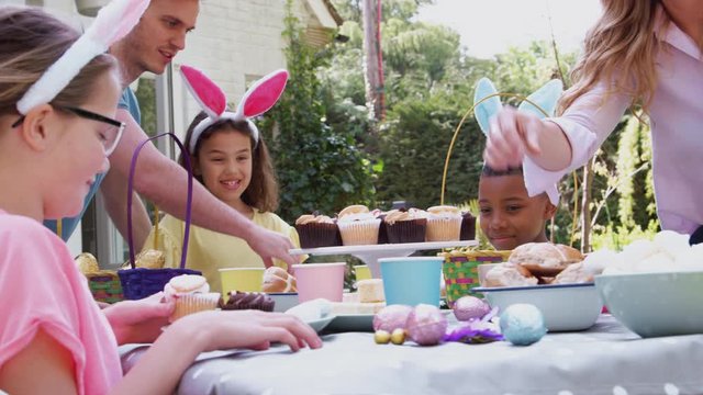 Parents With Children Wearing Bunny Ears Enjoying Outdoor Easter Party In Garden At Home