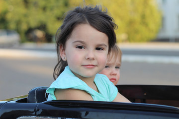 Two amazing girls ride in one big toy car on city street asphalt. Outdoor driving in a summer attraction for children