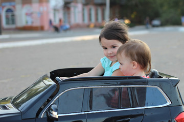 Two amazing girls ride in one big toy car on city street asphalt. Outdoor driving in a summer attraction for children